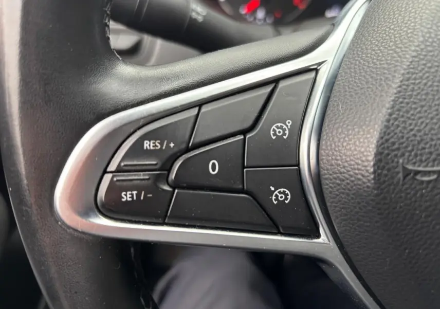 Gros plan sur les commandes du régulateur de vitesse au volant d'une Renault Clio gris foncé 2022.