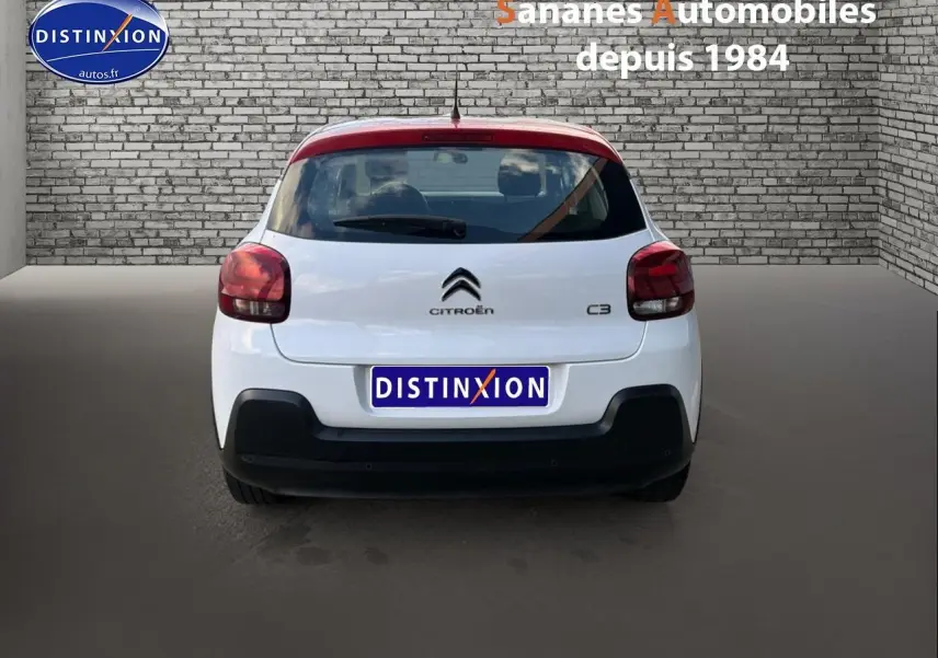 Vue arrière d'une Citroën C3 blanche de 2018 avec feux rouges et pare-chocs noir mat dans un décor urbain.