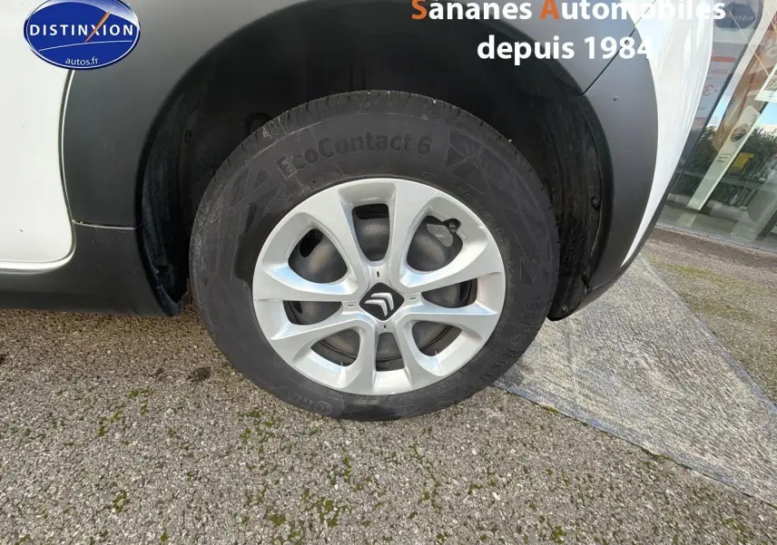 Gros plan sur la roue avant gauche d'une Citroën C3 blanche avec jante en alliage et passage de roue noir.