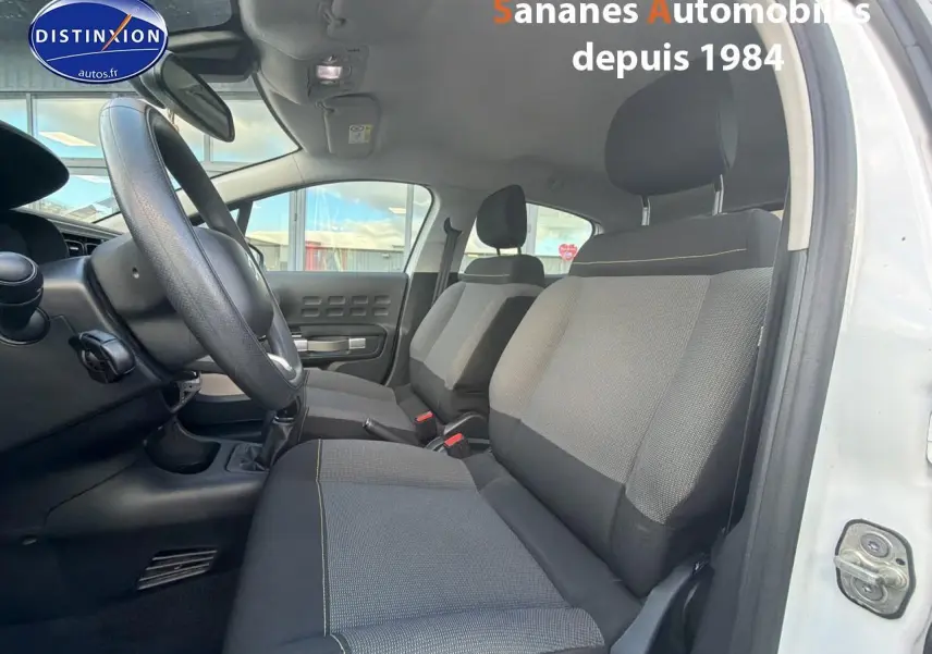 Vue intérieure côté conducteur de la Citroën C3 blanche 2018, sièges tissu gris avec surpiqûres jaunes visibles.