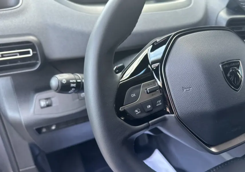 Gros plan sur le volant cuir multifonctions noir du Peugeot Rifter 2026 avec commandes intégrées et logo central.