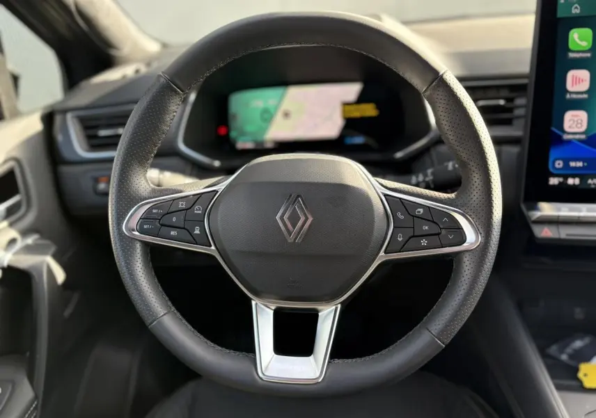 Vue rapprochée du volant noir perforé de la Renault SYMBIOZ 2025 avec commandes intégrées et logo central.