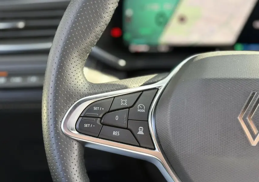 Gros plan sur le côté gauche du volant perforé gris du Renault Symbioz avec commandes de régulateur et assistant de conduite.