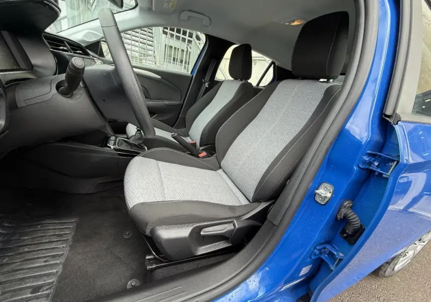 Intérieur côté conducteur d’une Opel Corsa bleu voltaik 2025, montrant les sièges avant gris et noirs et la boîte manuelle.