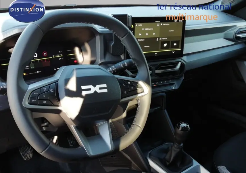 Vue intérieure du tableau de bord du Dacia Duster 2026 avec volant multifonction, écran tactile et levier de vitesse manuel.