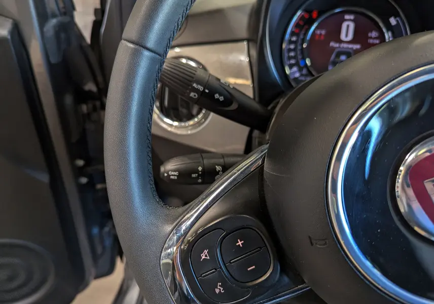 Gros plan sur le volant en cuir noir du Fiat 500 Electroclash Grey, avec commandes audio intégrées visibles.