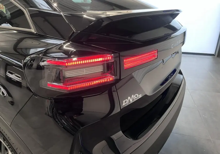 Feu arrière droit allumé et hayon noir métallisé d'une Citroën C4 hybride 2025 vue en 3/4 arrière.