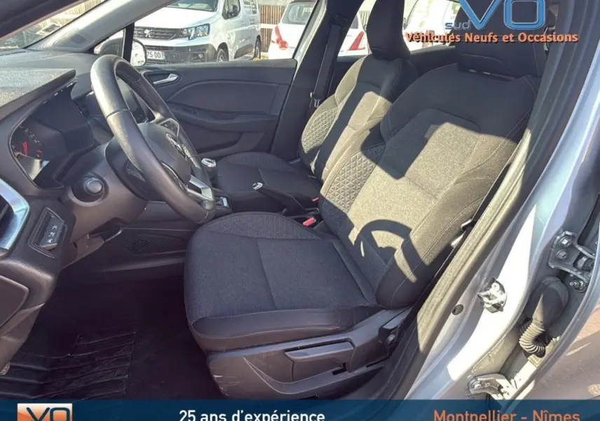 Intérieur côté conducteur de Renault Clio gris 2022, sièges tissu noir avec réglage hauteur et volant visible.