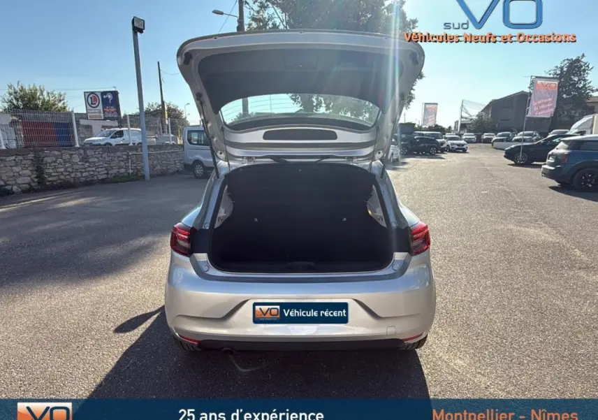 Vue arrière d'une Renault Clio gris clair 2022 avec coffre ouvert sur un parking ensoleillé