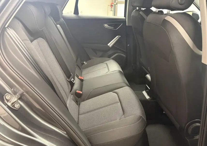 Vue intérieure côté gauche des sièges arrière en tissu gris de l'Audi Q2 35 TFSI S Line 2026 avec portière ouverte.