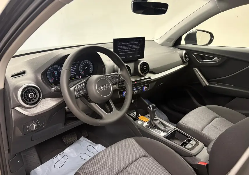 Vue intérieure côté conducteur de l'Audi Q2 35 TFSI 150 S tronic 7 S line avec tableau de bord moderne et sièges gris.