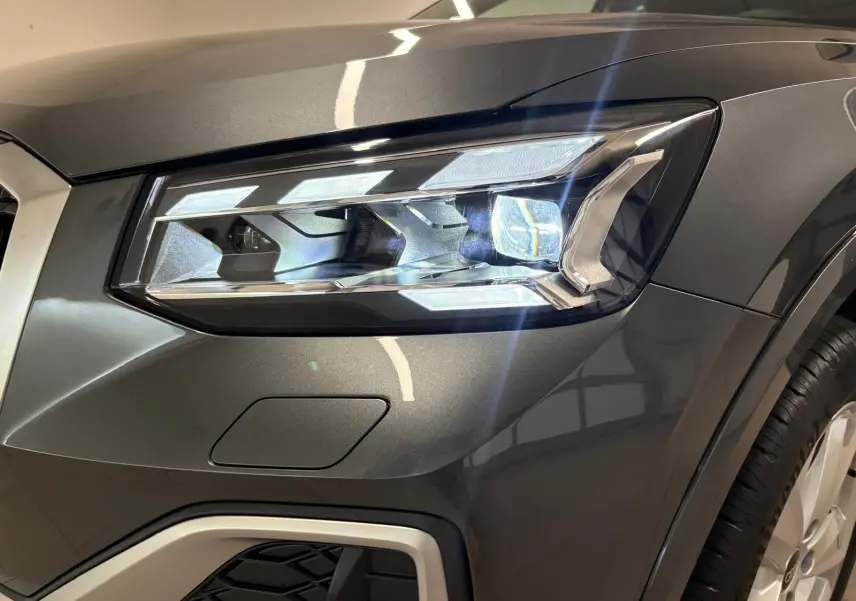 Gros plan sur le phare avant droit de l'Audi Q2 35 TFSI S Line en Gris Daytona métallisé, avec détails lumineux nets.