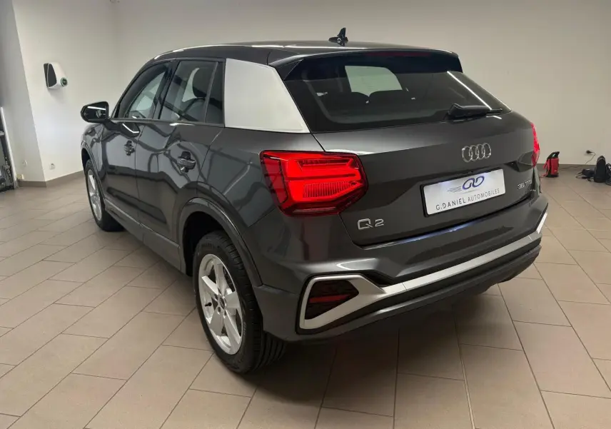 Vue 3/4 arrière droite de l'Audi Q2 35 TFSI S Line gris Daytona avec toit noir et montant arrière argenté.