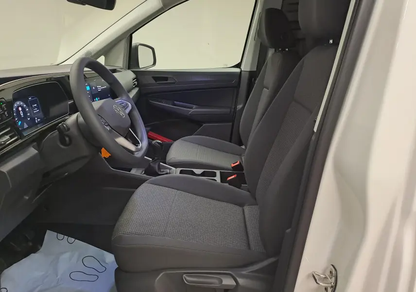 Intérieur côté conducteur du Volkswagen Caddy Cargo Maxi blanc, vue de profil montrant sièges noirs et tableau de bord numérique.
