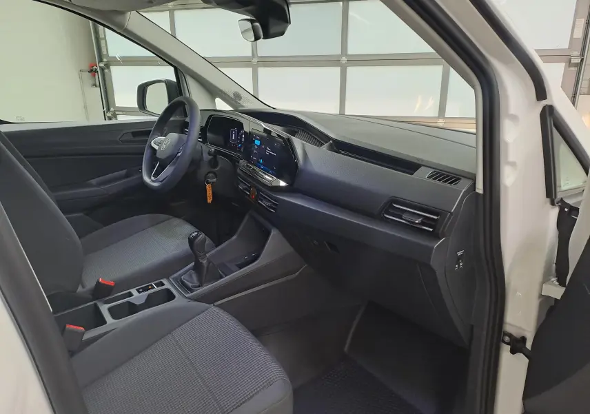 Vue intérieure côté conducteur du Volkswagen Caddy Cargo Maxi blanc Candy 2026, avec tableau de bord moderne et boîte manuelle.