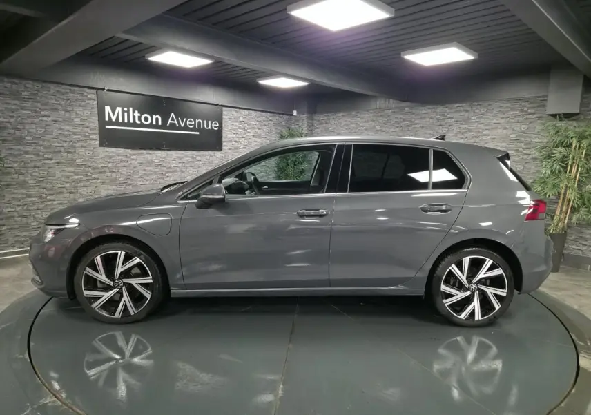 Profil côté gauche d'une Volkswagen Golf gris Urano avec jantes alliage 18 pouces dans un showroom intérieur.