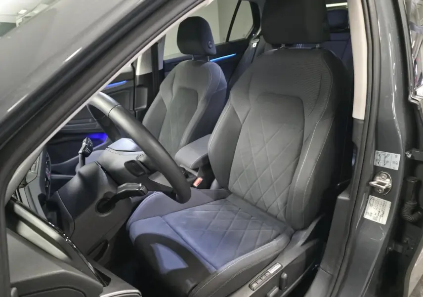 Vue intérieure côté conducteur de la Volkswagen Golf gris avec sièges sport confort et éclairage d'ambiance bleu.