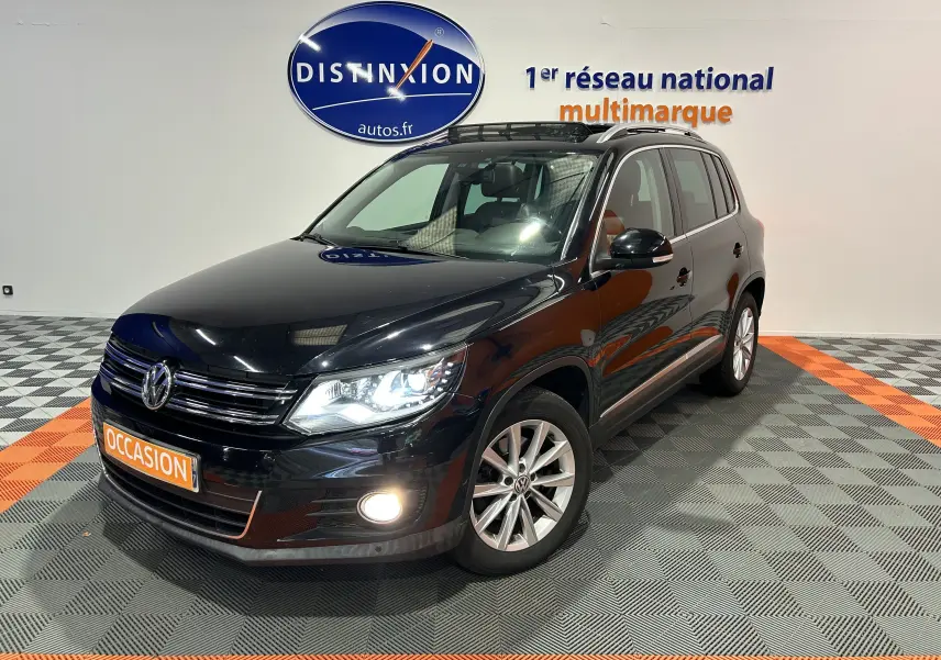 Volkswagen Tiguan noir métal 2015 en 3/4 avant droit avec phares et antibrouillard allumés, toit ouvrant visible.