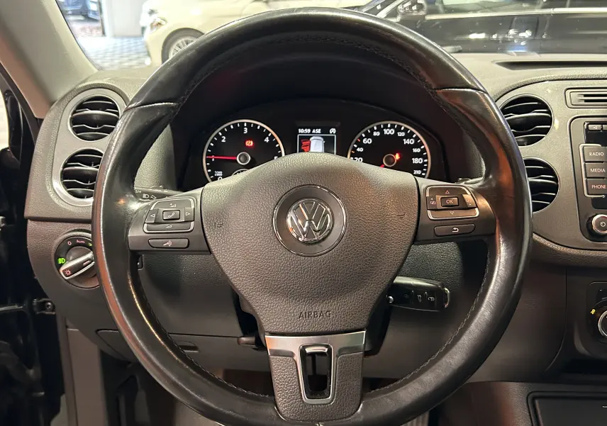 Vue rapprochée du volant en cuir noir du Volkswagen Tiguan 2015 avec commandes intégrées et tableau de bord visible.
