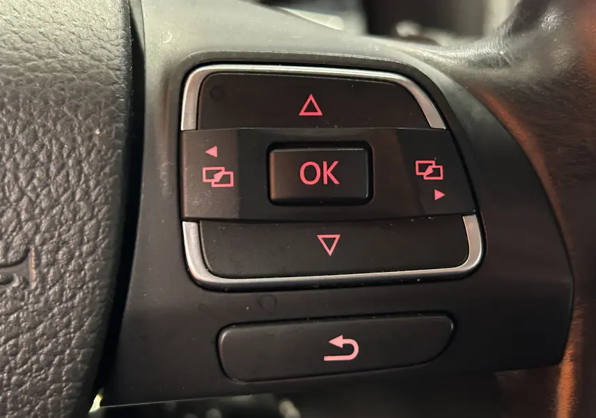 Gros plan sur les commandes de direction au volant du Volkswagen Tiguan 2015 noir métal avec boutons rétroéclairés rouges.