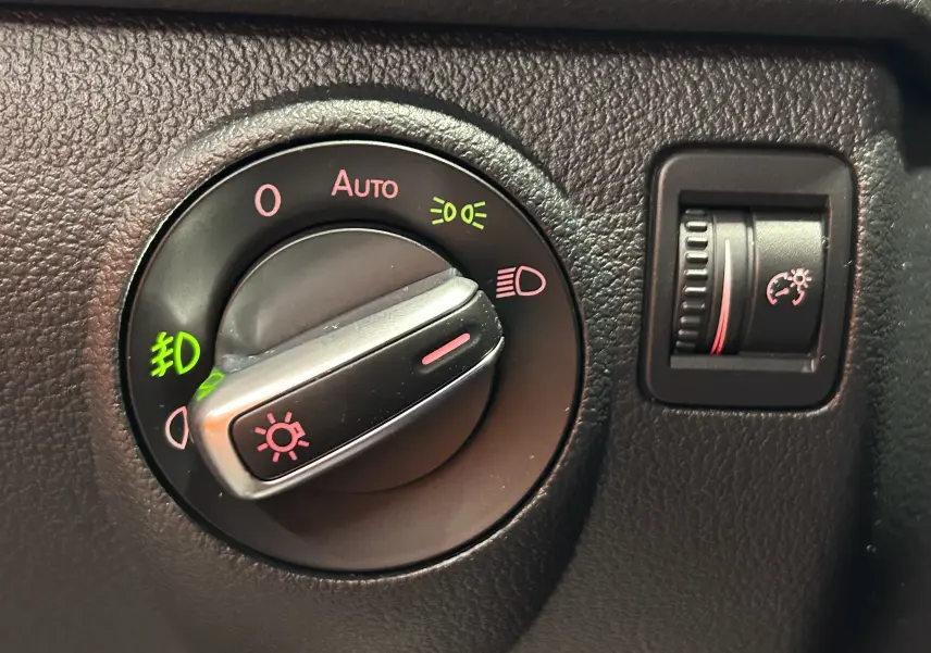 Gros plan sur la molette de réglage des phares et le variateur de luminosité du tableau de bord du Volkswagen Tiguan noir métal.