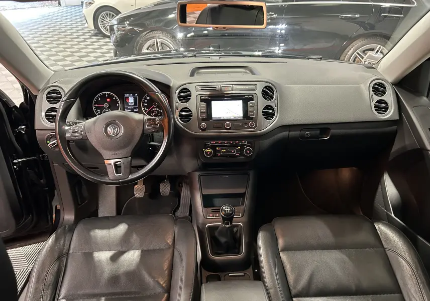 Vue intérieure avant du Volkswagen Tiguan 2.0 TDI 2015 avec sièges cuir noirs, volant multifonction et boîte manuelle.