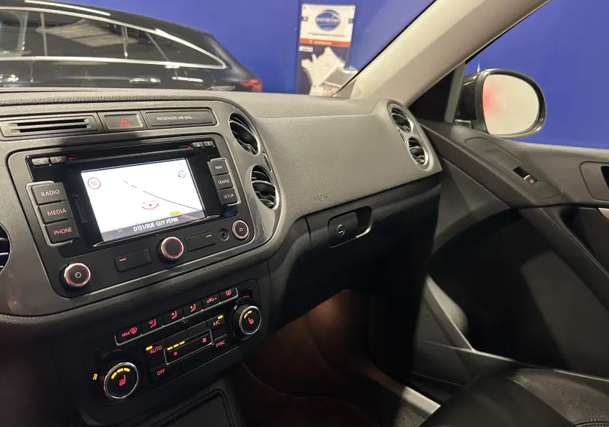 Intérieur côté passager du Volkswagen Tiguan noir métal 2015, tableau de bord avec écran GPS et commandes climatisation.