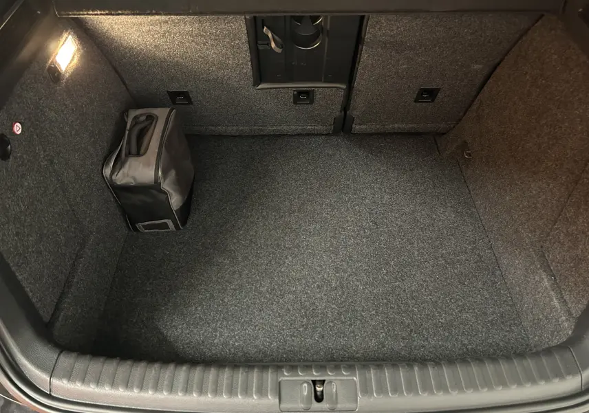 Coffre propre et spacieux du Volkswagen Tiguan noir métal, avec sac de rangement et éclairage intérieur allumé.