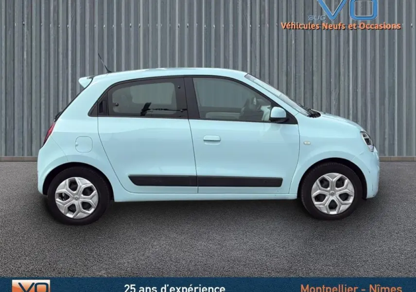Profil côté gauche d'une Renault Twingo III Zen bleu clair, compacte et urbaine, sur fond industriel neutre.
