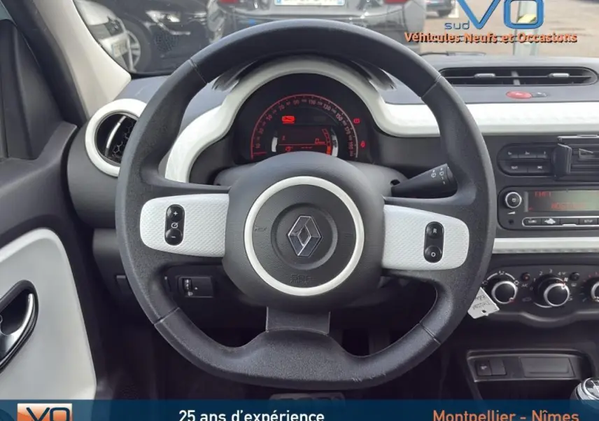 Vue intérieure centrée sur le volant noir et blanc de la Renault Twingo III bleu clair, tableau de bord et commandes visibles.