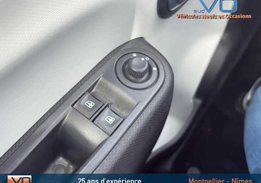 Gros plan sur les commandes des vitres électriques et réglage des rétroviseurs côté conducteur d'une Renault Twingo III bleu clair.