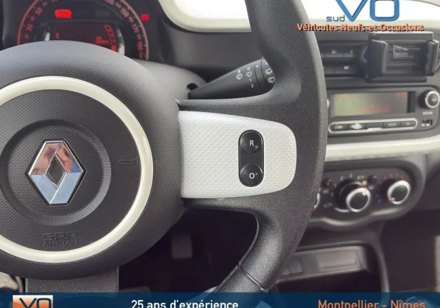 Vue rapprochée du volant noir et blanc de la Renault Twingo III bleu clair avec tableau de bord et commandes visibles.