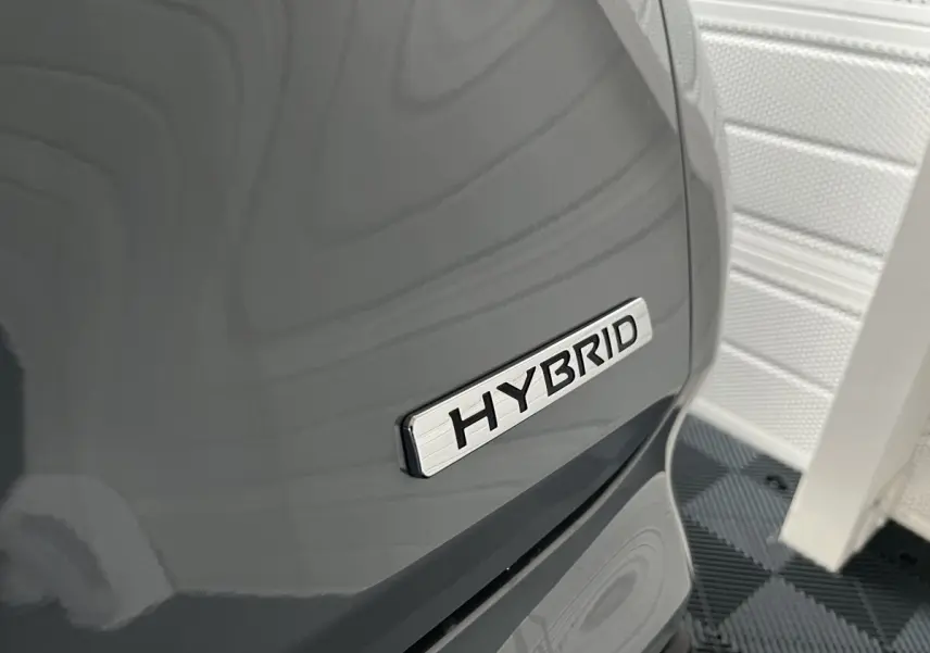 Gros plan sur l’inscription Hybrid sur la portière côté droit d’un Nissan Juke gris clair 2024.