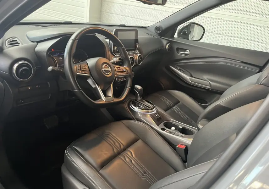 Vue intérieure côté conducteur du Nissan Juke Hybrid 2024, sièges cuir noirs et tableau de bord avec écran tactile central.