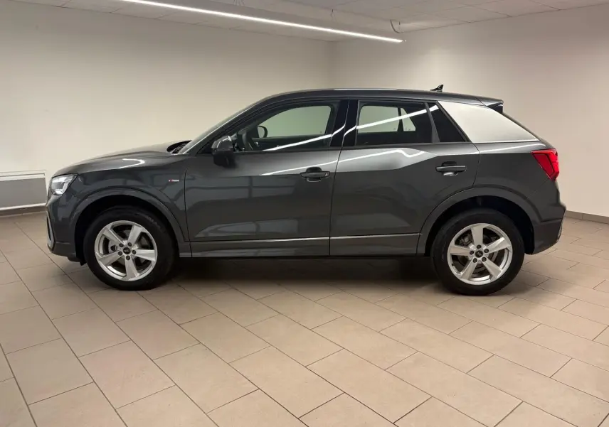 Audi Q2 35 TFSI S Line gris Daytona vu de profil côté gauche dans un intérieur neutre.