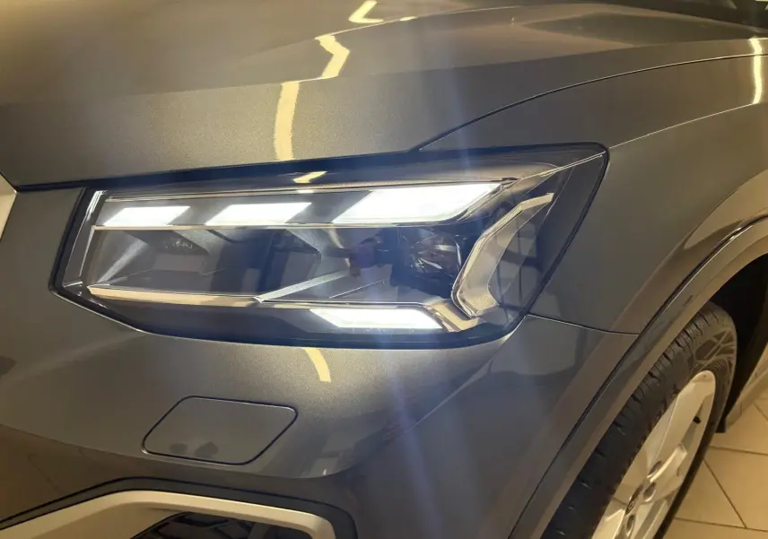 Gros plan sur le phare avant droit allumé d’un Audi Q2 35 TFSI S Line gris Daytona avec peinture métallisée.