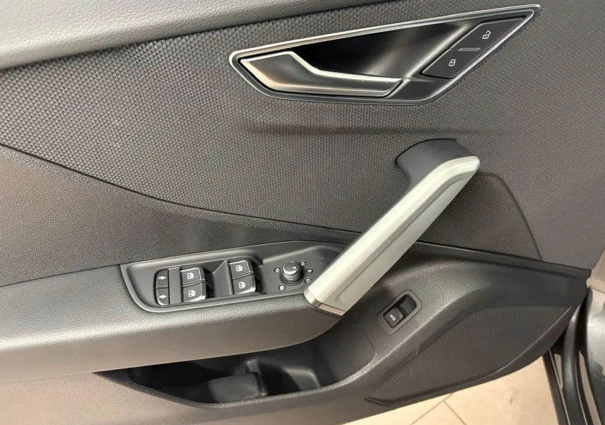 Gros plan sur la porte côté conducteur de l'Audi Q2 35 TFSI S Line 2026 en Gris Daytona, montrant les commandes de vitres et la poignée argentée.