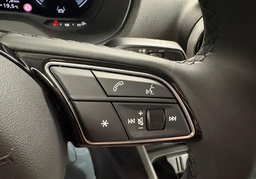 Gros plan sur les commandes multifonctions au volant de l'Audi Q2 35 TFSI S Line gris Daytona, tableau de bord en arrière-plan.