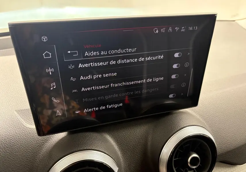 Écran central intérieur de l'Audi Q2 35 TFSI 150 S Line 2026 affichant les aides à la conduite, avec aérateurs ronds en dessous.