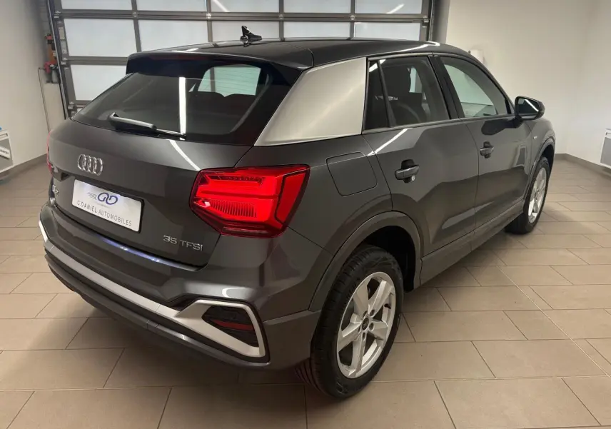 Audi Q2 35 TFSI S Line gris Daytona vue 3/4 arrière droit en intérieur, feux arrière allumés.