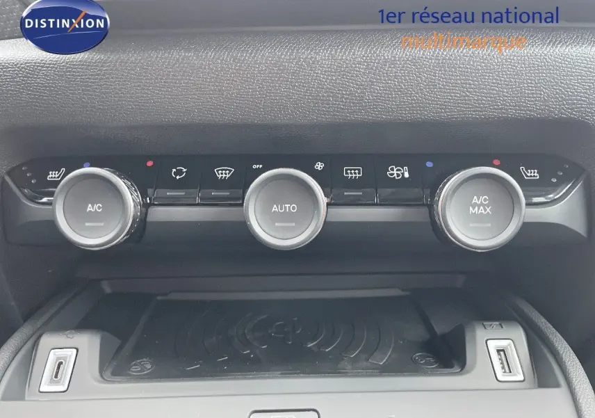 Vue rapprochée de la console centrale de la Citroën C4 blanche, montrant les commandes de climatisation et un chargeur sans fil.