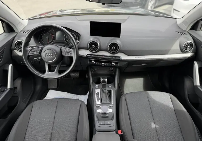 Intérieur Audi Q2 2022 vu de face, tableau de bord gris avec volant cuir noir et console centrale moderne.