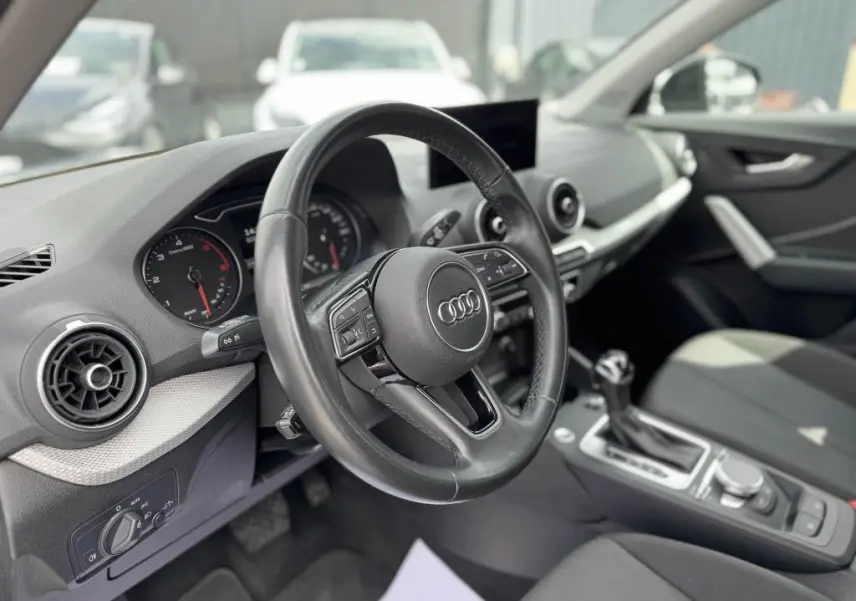 Intérieur noir d'Audi Q2 2022 vu côté conducteur, volant cuir multifonction et console centrale avec boîte auto.