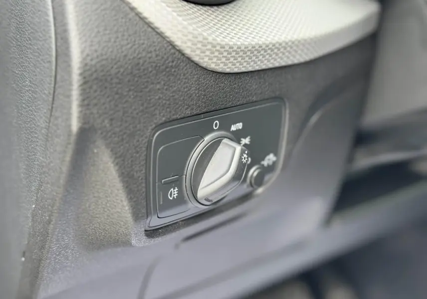 Gros plan sur le bouton de commande des phares dans l'habitacle noir de l'Audi Q2 2022 Design Diesel.