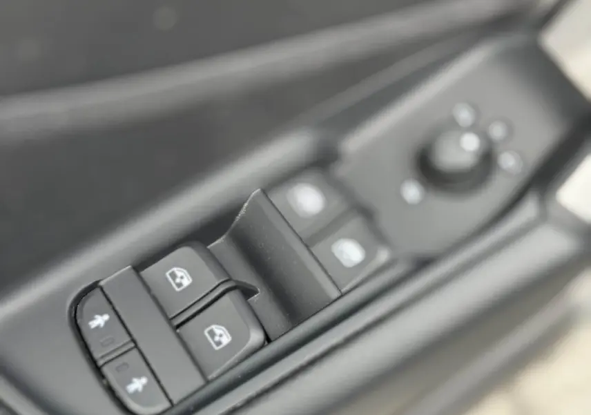 Gros plan sur les commandes des vitres électriques et rétroviseurs côté gauche d'un Audi Q2 noir 2022.
