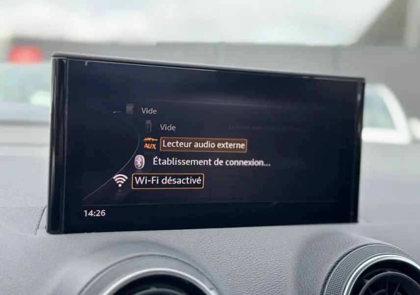 Écran central de l'Audi Q2 noir 2022 affichant les options audio et Wi-Fi désactivé, entouré de la console grise.