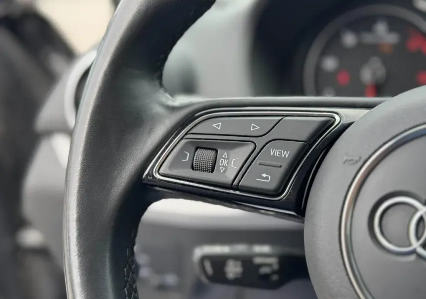 Gros plan sur les commandes gauche du volant cuir noir de l'Audi Q2 2022 avec boutons multifonctions et molette.