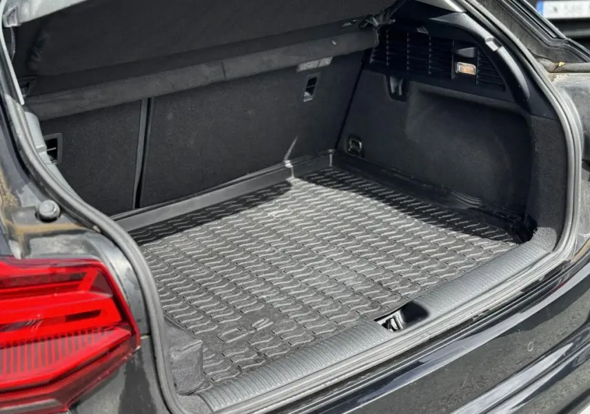 Coffre ouvert vu de l'arrière gauche d'un Audi Q2 noir avec tapis de coffre en caoutchouc et feux arrière LED rouges.