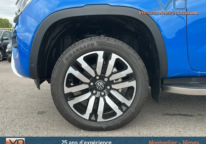 Gros plan sur la roue avant gauche du Volkswagen Amarok bleu 2025 avec jante alliage 21 pouces et marchepied visible.