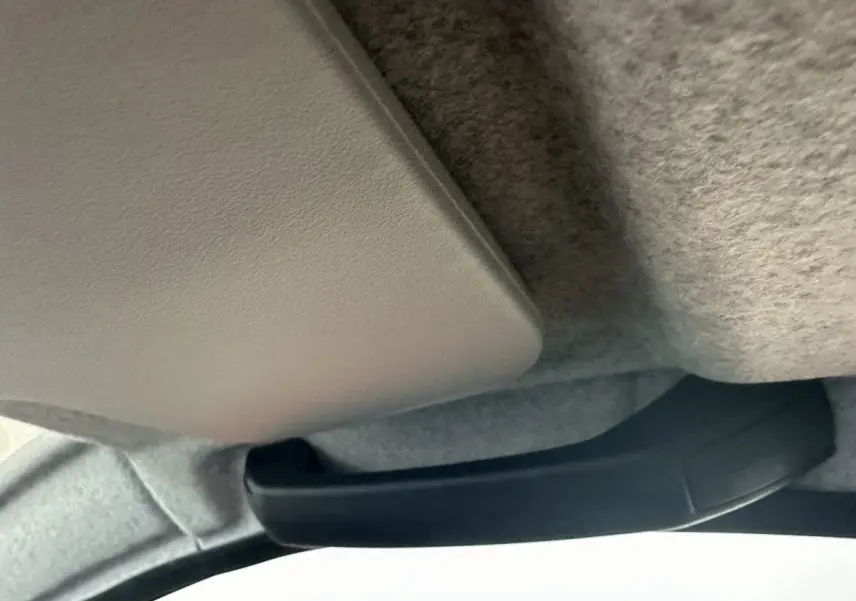 Poignée de maintien noire fixée au plafond intérieur d'un véhicule, avec revêtement gris clair en tissu.